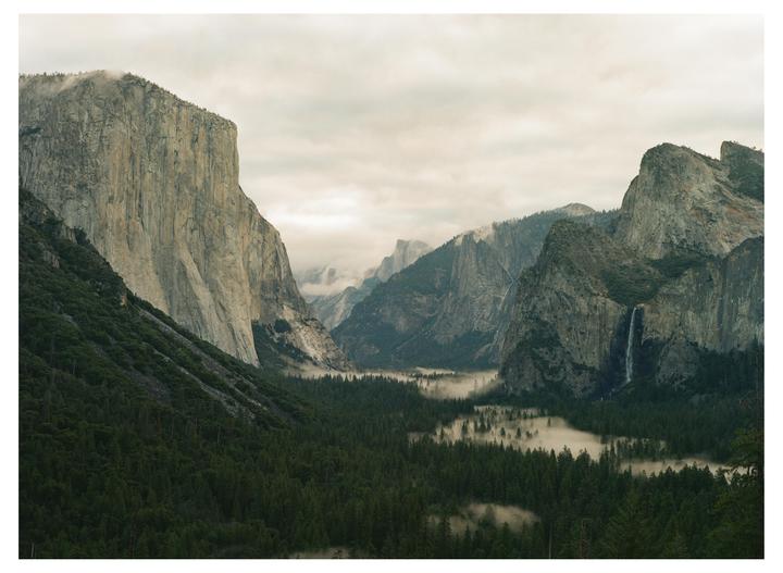 A foggy morning in a valley with tall mountains and a waterfall.