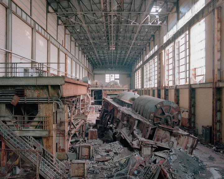 A large, abandoned power plant interior is filled with debris and rusting machinery.