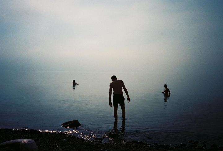 Three people are wading in a body of water with a hazy sky.