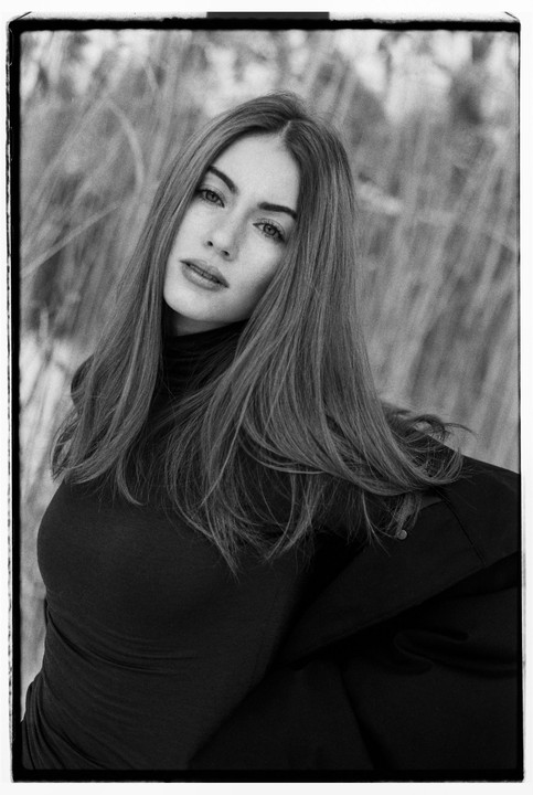 A woman with long hair and a dark top looks at the viewer in a black and white portrait.
