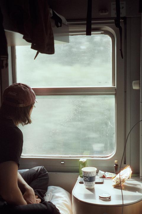 A person wearing a baseball cap looks out a train window at a passing landscape.