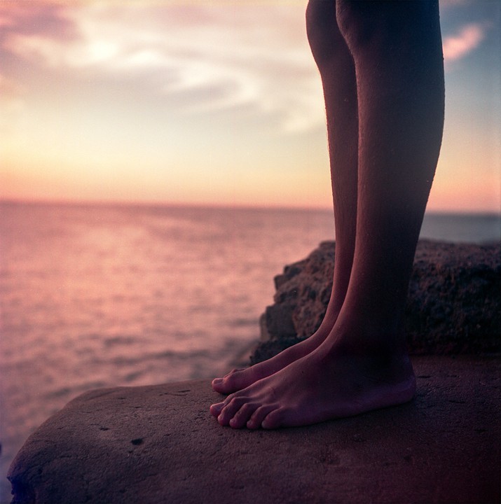 A person stands on a rock overlooking the ocean at sunset.