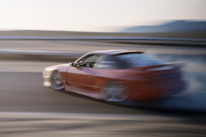 A red sports car drifts on a track, creating a cloud of smoke behind it.