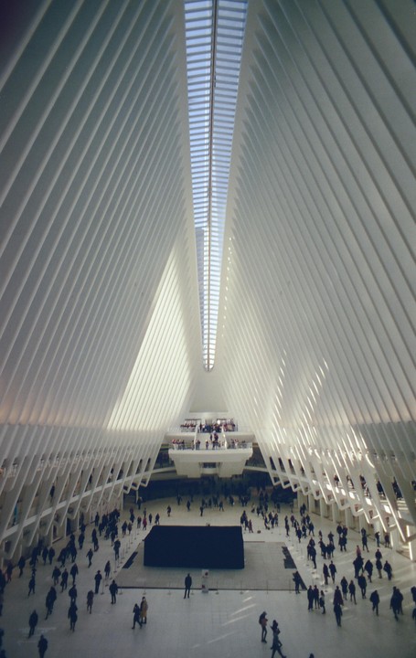 A large, modern, white building with a high ceiling and many people walking around inside.