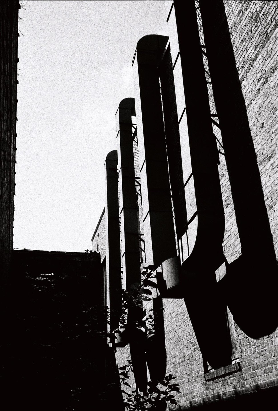 Tall, dark pipes cast long shadows on a brick building under a bright sky.