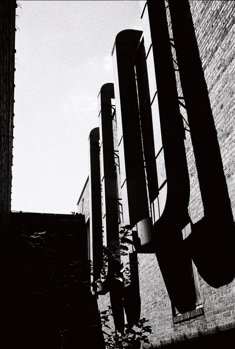 Tall, dark pipes cast long shadows on a brick building under a bright sky.
