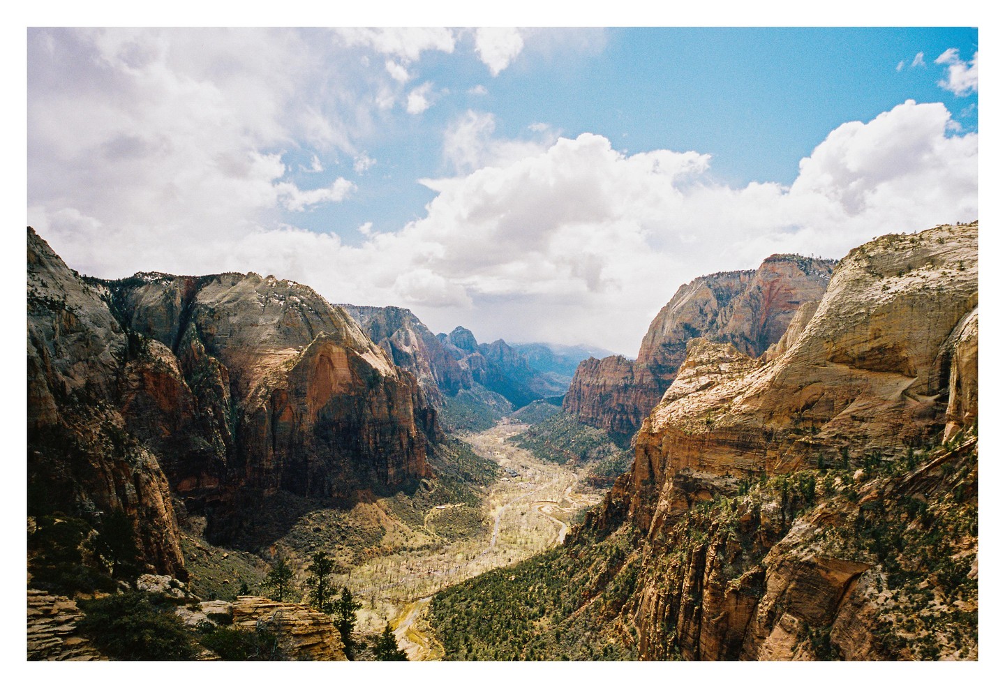 A wide valley with a winding river is visible between two large mountains under a cloudy sky.