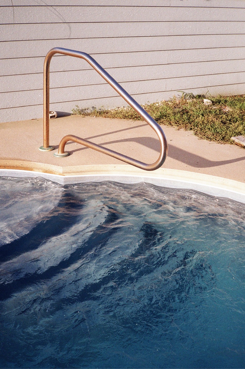 A metal handrail extends into a swimming pool with blue water.