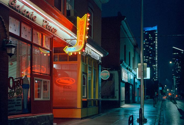 A diner with a neon sign is visible on a city street at night.