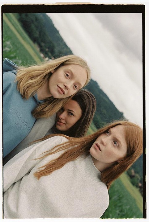 Three women pose for a portrait on a grassy hillside under a cloudy sky.