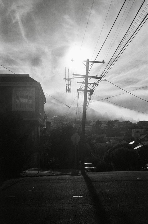 A street scene shows a utility pole and power lines in the foreground, with a building on the left and a hazy cityscape in the background.