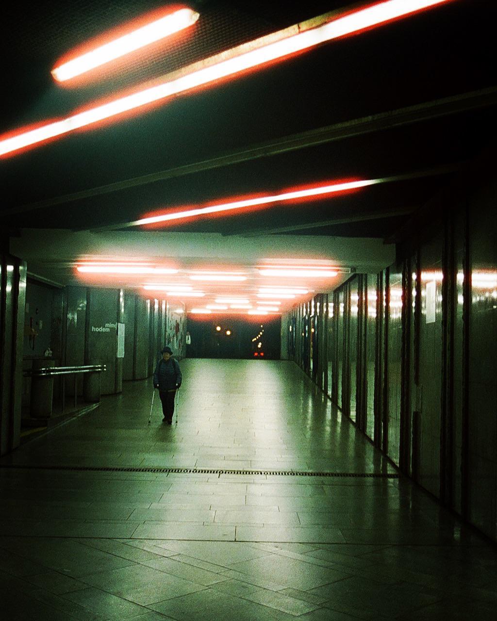 A person with a cane walks down a long, brightly lit underground passageway.