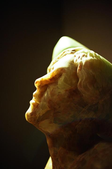 A marble bust of a man is illuminated from above, highlighting the details of his face and the texture of the stone.