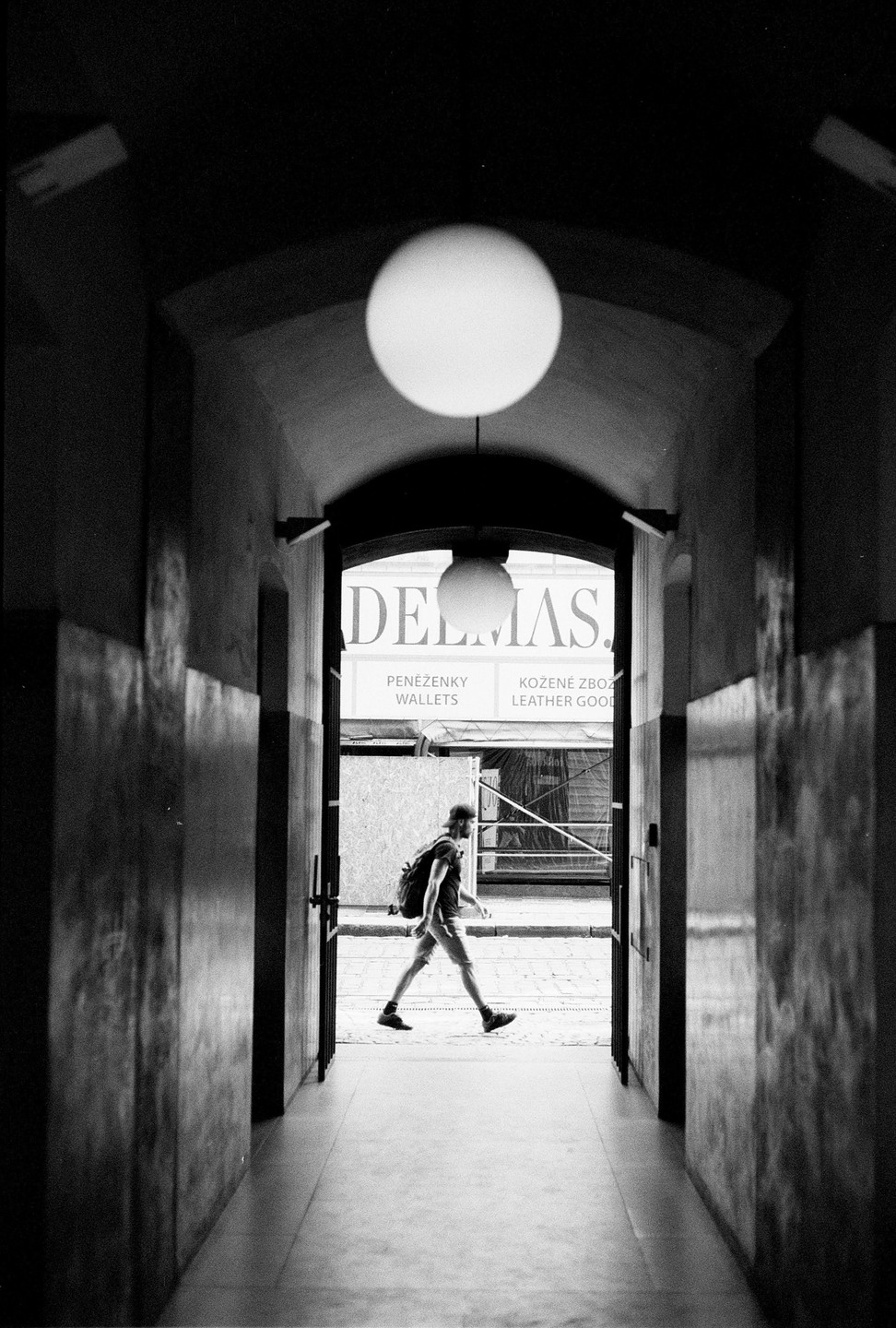 A man with a backpack walks through a doorway with a large round light fixture overhead.
