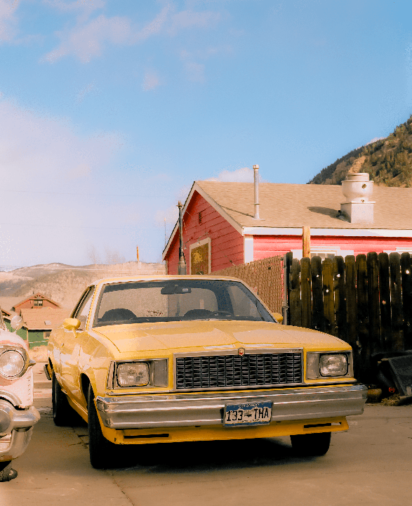 A yellow car is parked in front of a red building with a mountain in the background.