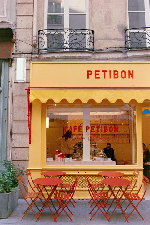 A yellow cafe with red tables and chairs outside is visible from the street.