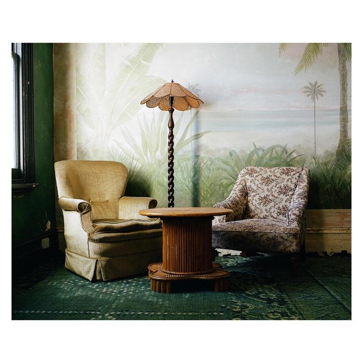 Two armchairs and a small table are arranged in a room with a tropical mural on the wall.