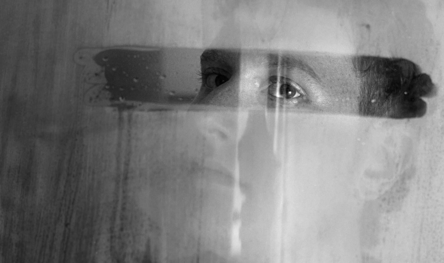 A woman's eyes are visible through a steamy, wet surface, with her face partially obscured by condensation.