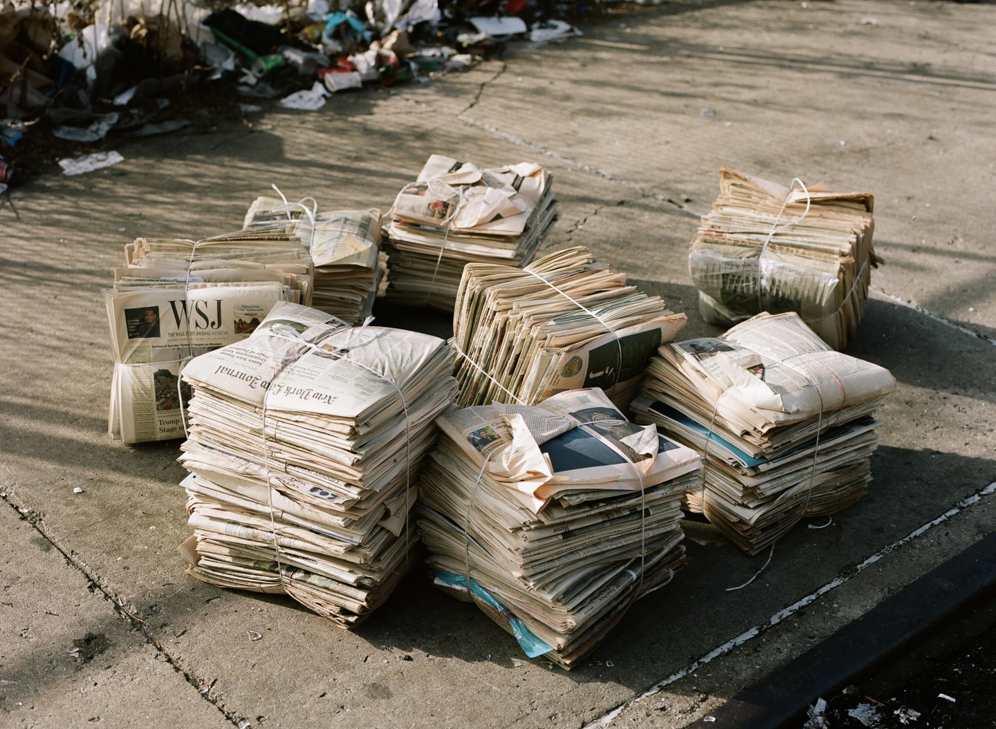Bundles of old newspapers are stacked on a concrete surface.
