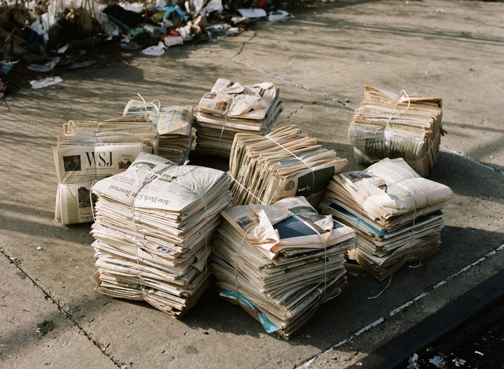Bundles of old newspapers are stacked on a concrete surface.