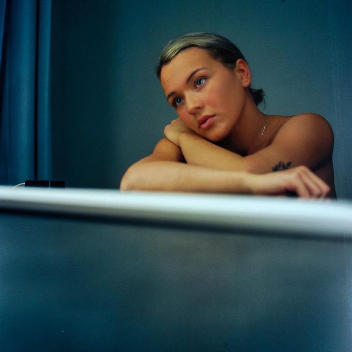 A woman with her arms crossed is resting her head on her arms and looking up and to the right.