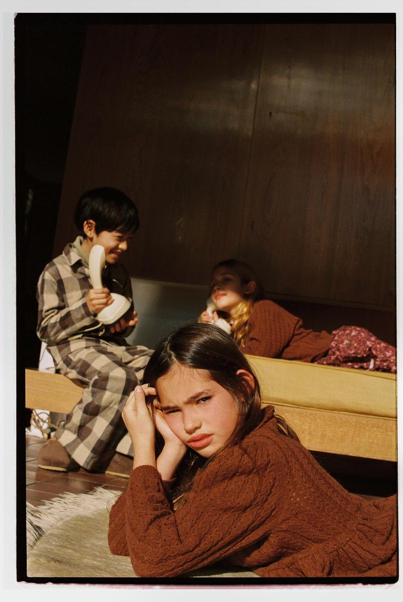 Three children are playing with toy telephones in a sunlit room.