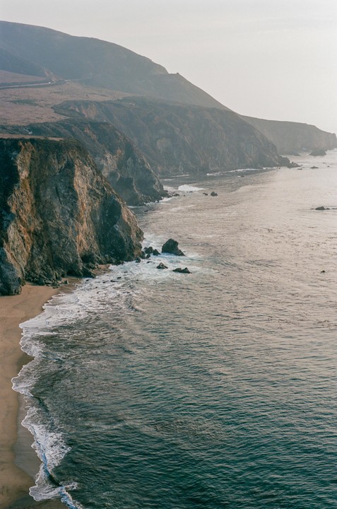 A long stretch of coastline with cliffs, a sandy beach, and the ocean with waves.