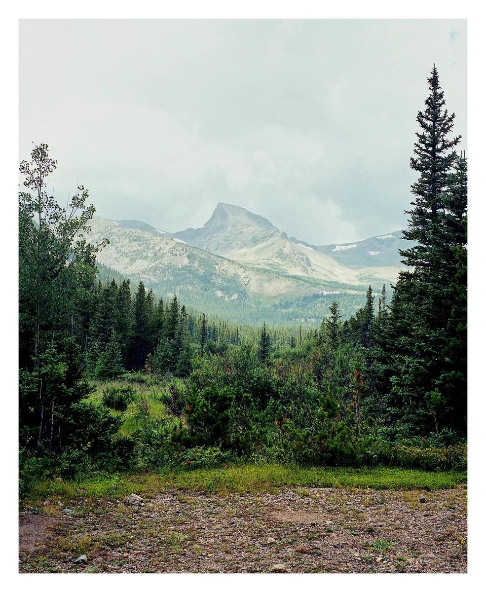 A mountain peak rises above a dense forest under a cloudy sky.