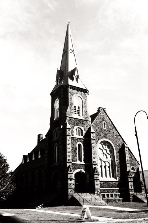 A tall stone church with a prominent steeple stands under a bright sky.
