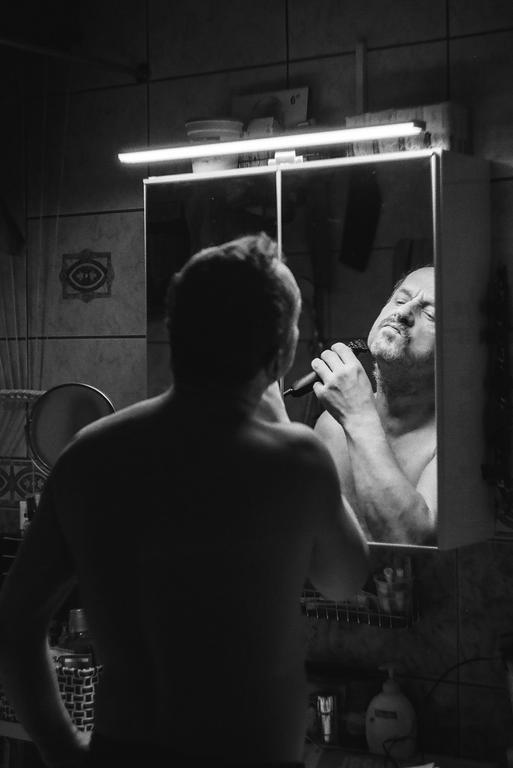 A man shaves his beard in a mirror in a bathroom.
