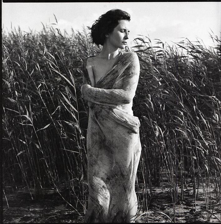 A woman wrapped in fabric stands in a field of tall reeds.
