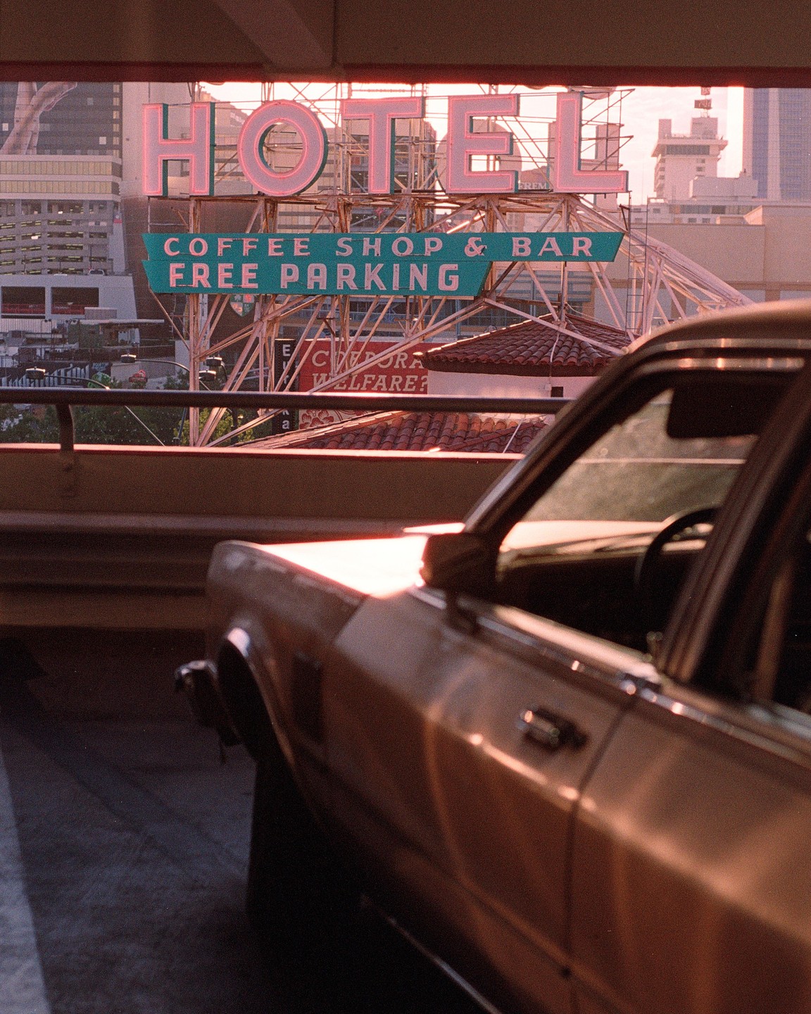 A car is parked in front of a hotel sign that also advertises a coffee shop, bar, and free parking.
