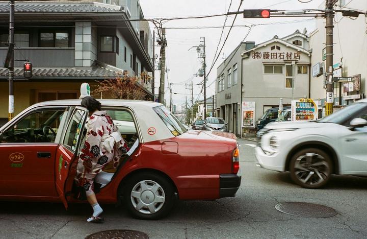 A woman in a kimono steps out of a red taxi onto a city street.
