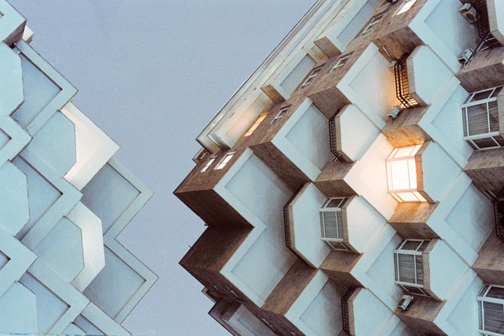 Two buildings with geometric patterns on their facades are seen from a low angle against a light sky.