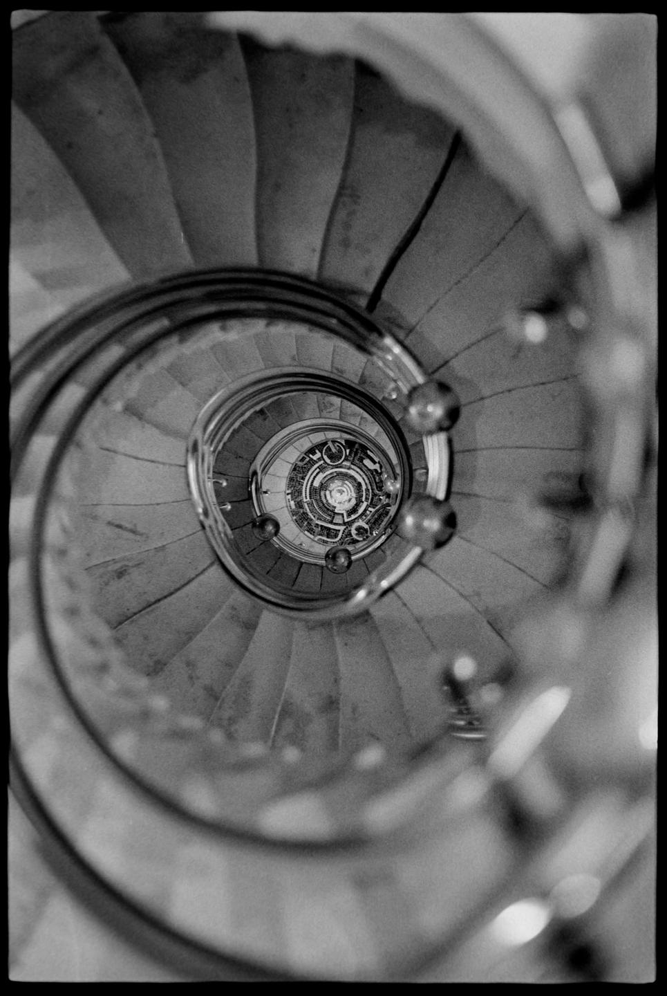 A spiral staircase with a metal railing descends into the distance, viewed from above.