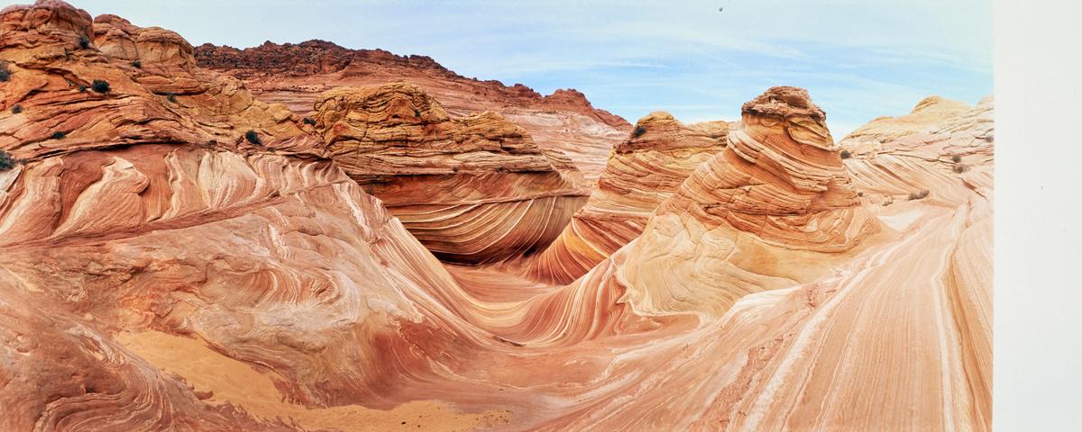 A panoramic view shows a desert landscape with swirling rock formations under a blue sky.