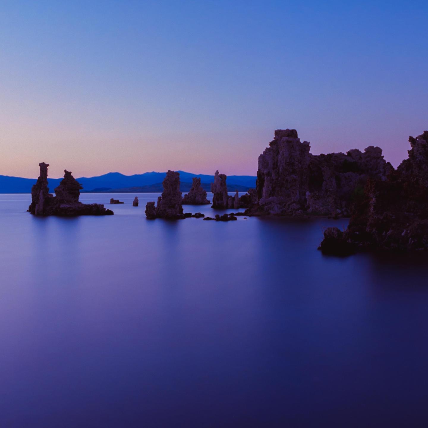 Tufa formations rise from the still water of Mono Lake under a blue hour sky.