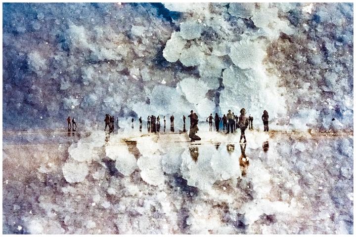 A group of people stand on a reflective surface under a textured sky.