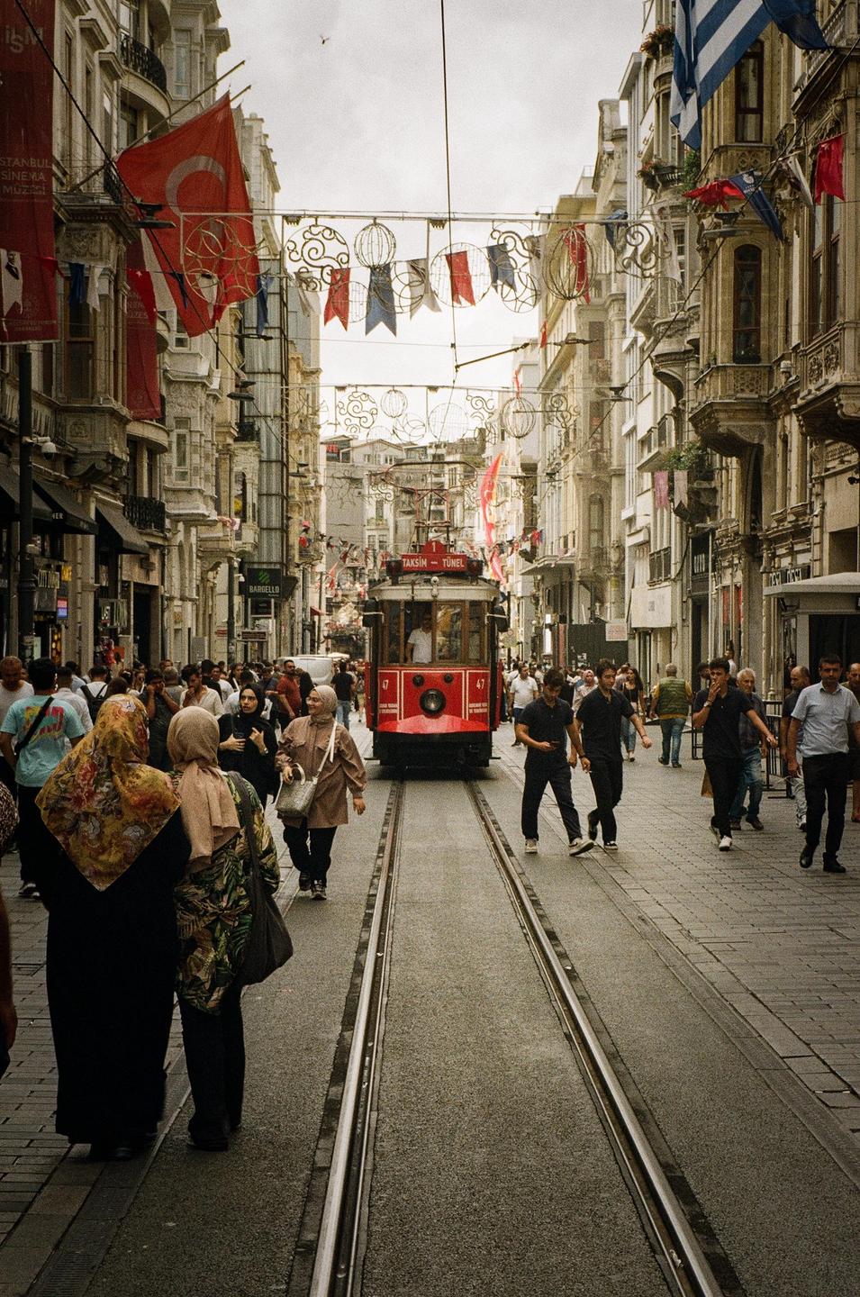 A red tram travels down a street lined with tall buildings and people.
