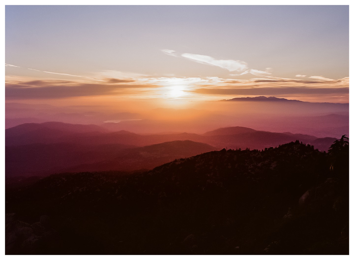 The sun sets over a mountain range with a hazy sky.