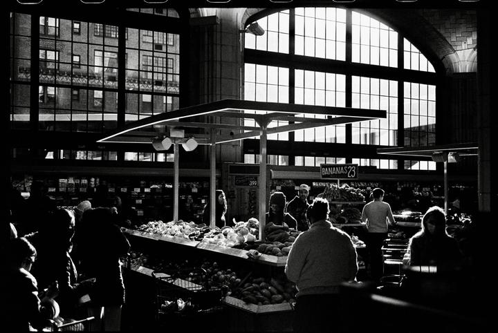 People are shopping for produce in a market with large windows.