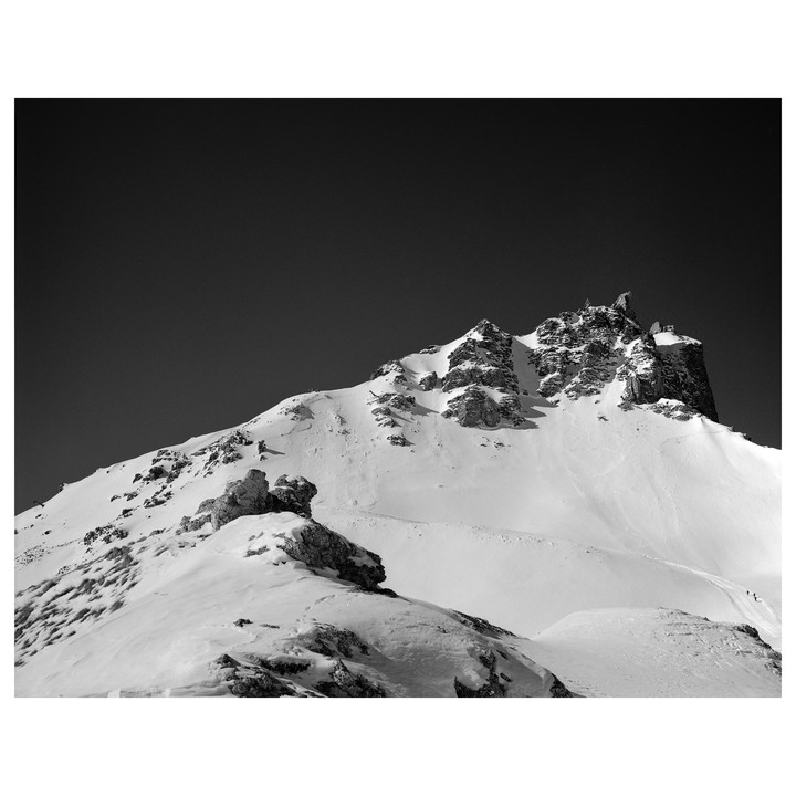 A snow-covered mountain peak rises against a dark sky, with a small group of people visible on the slope.