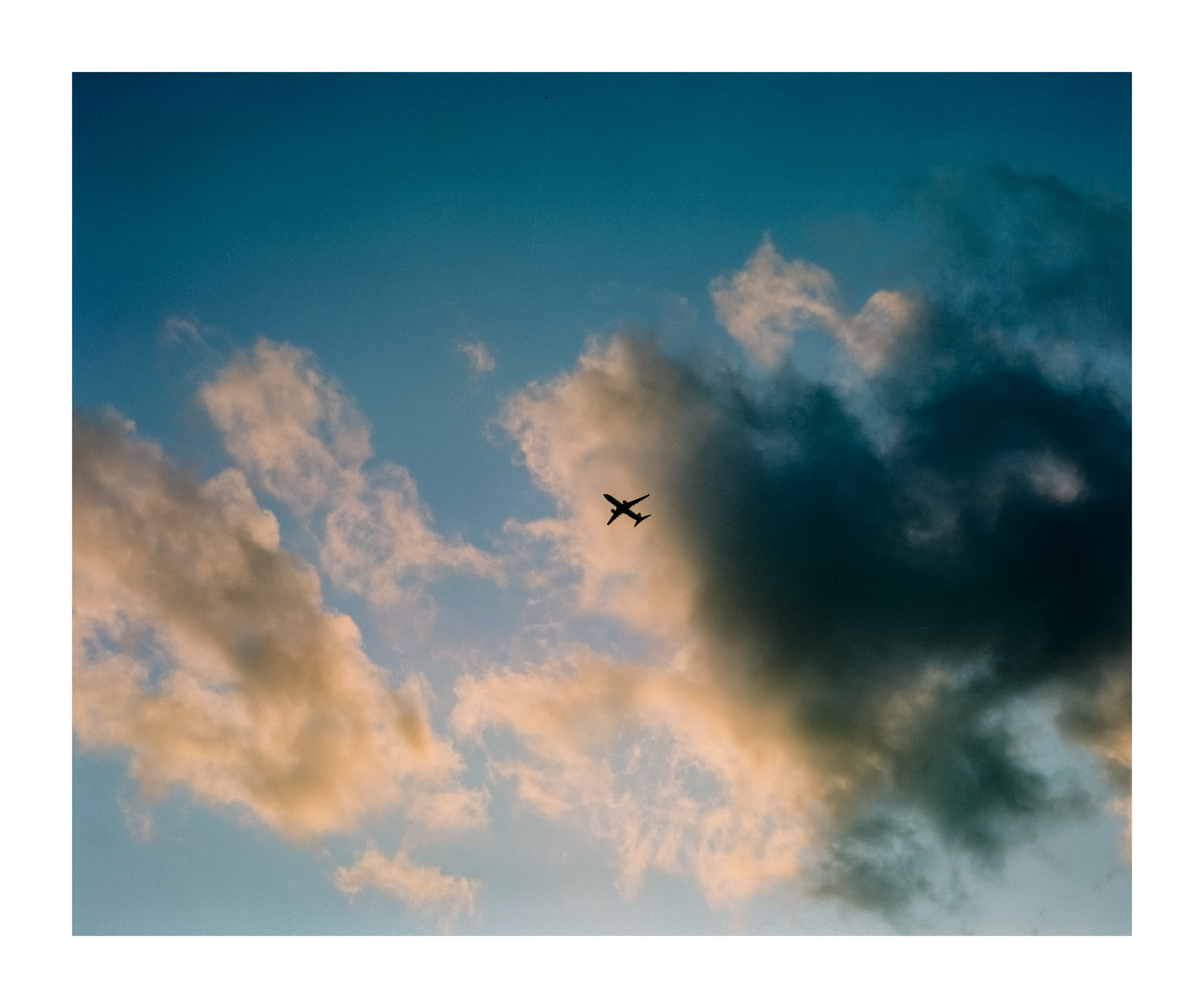 A silhouette of an airplane flies across a partly cloudy sky.