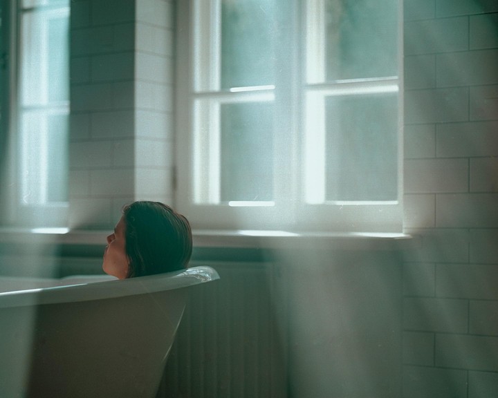 A woman is relaxing in a bathtub with light rays coming through a window.