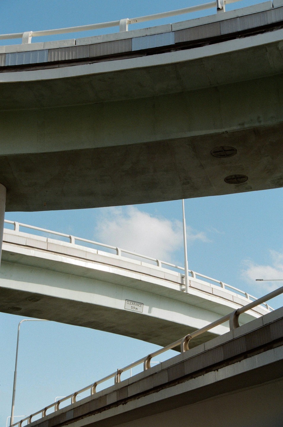 Three concrete overpasses with railings curve across a blue sky with a single cloud.