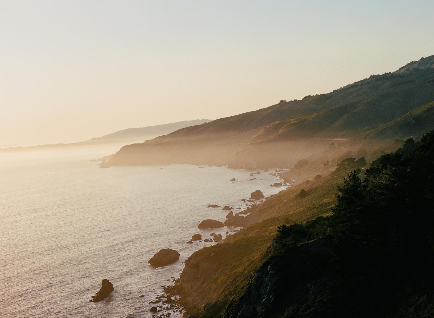 A hazy coastline with mountains and trees is visible at sunset.