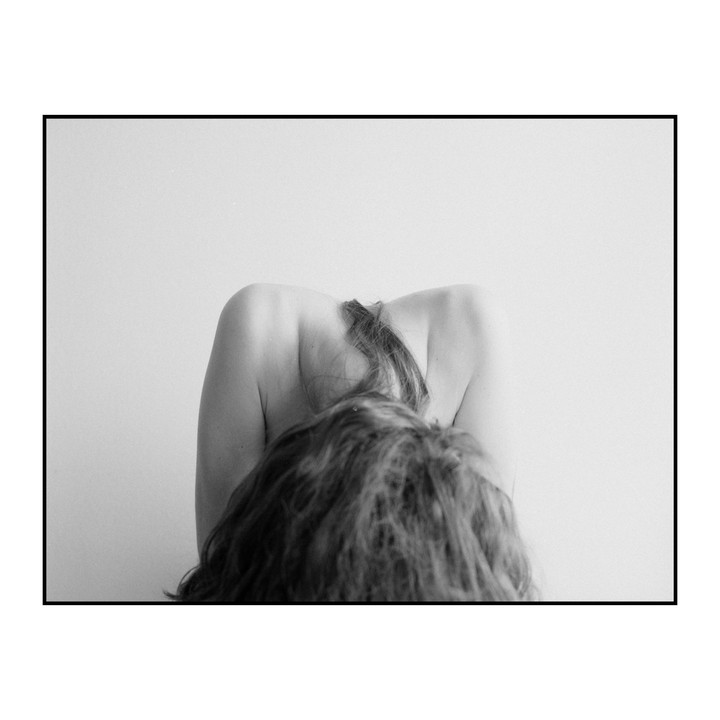 A woman with long hair is seen from behind, bending forward with her back exposed.