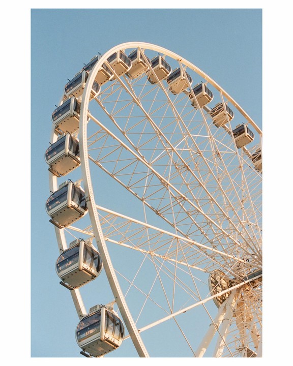 A large white ferris wheel with many gondolas is set against a clear blue sky.