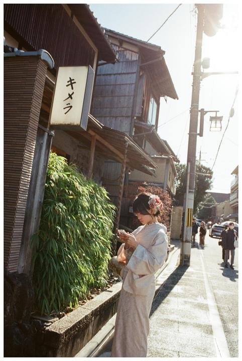 A woman in a kimono stands on a street in Kyoto, looking at her phone.
