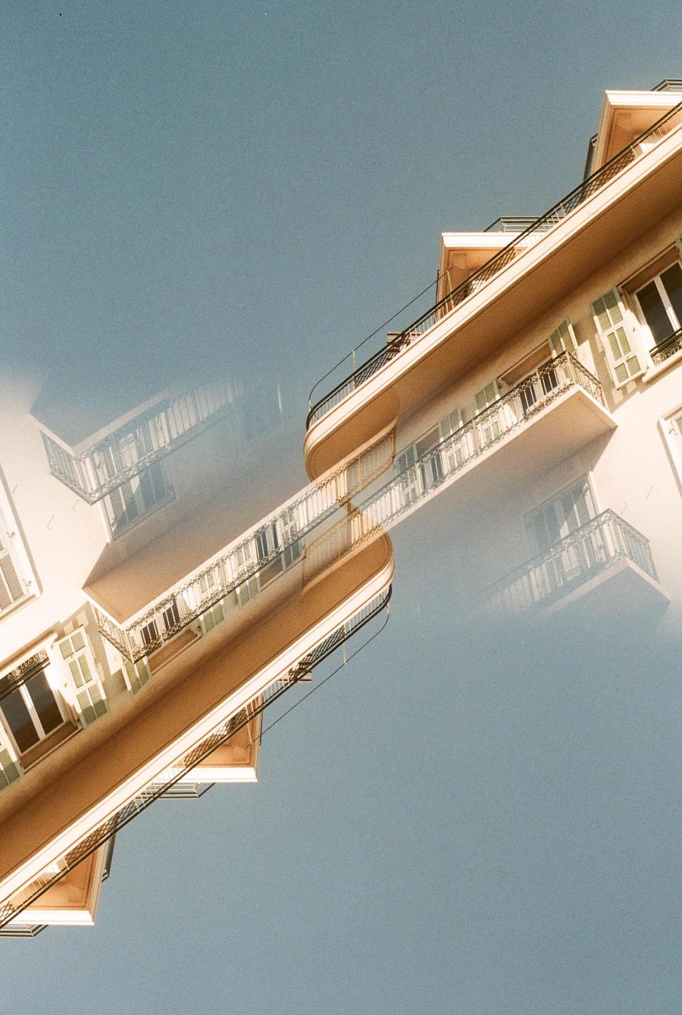 A double exposure shows a building with balconies and windows against a clear sky.
